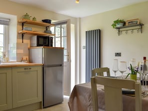 A kitchen with a refrigerator, microwave, and wooden shelves. There is a dining table with chairs and a window with blinds. - Keldholme Cottages 2 - UK11488 (Keldholme, near Kirkbymoorside)
