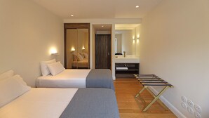A hotel room with two beds, a small seating area, a mirror, and a wooden floor.