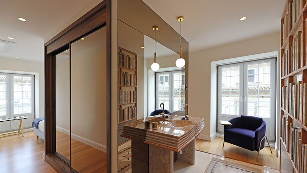 A modern bathroom with a large mirror, a double sink, and a bookshelf.