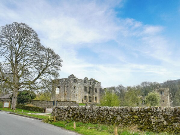 A historic stone building with a large tree in the foreground, a stone wall, and a clear sky. - 1 bedroom accommodation in Skipton (Skipton)
