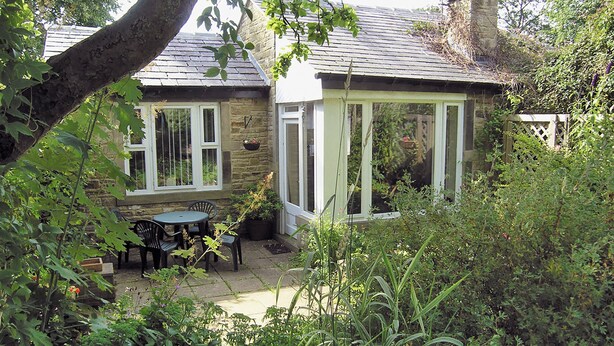 Una casa de piedra con un patio, una zona de estar cubierta y un jardín.