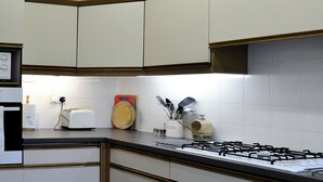 Una cocina con gabinetes blancos, estufa a gas, tostadora y diversos utensilios de cocina.