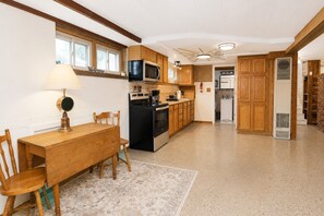 A kitchen with wooden cabinets, a microwave, stove, and a dining area with a table and chairs.
