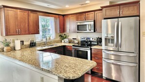 A modern kitchen with granite countertops, stainless steel appliances, wooden cabinets, and a window with a view of greenery.