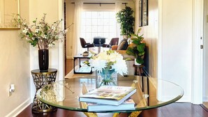 A dining area with a glass table, a geometric pendant light, and a woven rug.