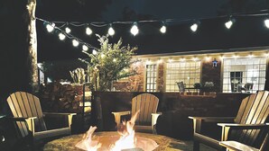 An outdoor patio with a fire pit, chairs, and string lights.