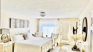 A bedroom with a large bed, a nightstand, a chair, a dresser, a mirror, and a window with curtains.