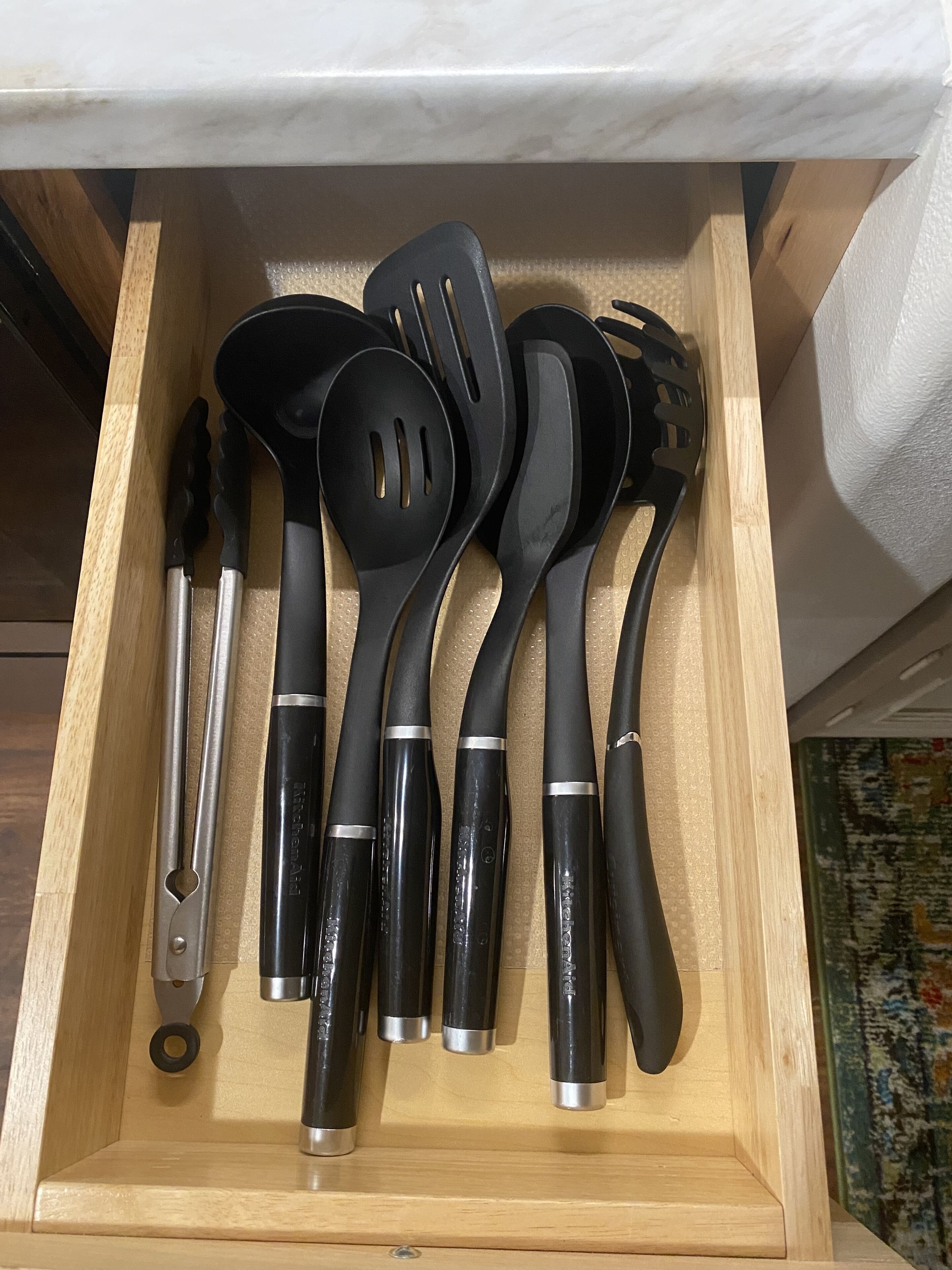 Un tiroir contenant divers ustensiles de cuisine, notamment une spatule, une écumoire et une louche.