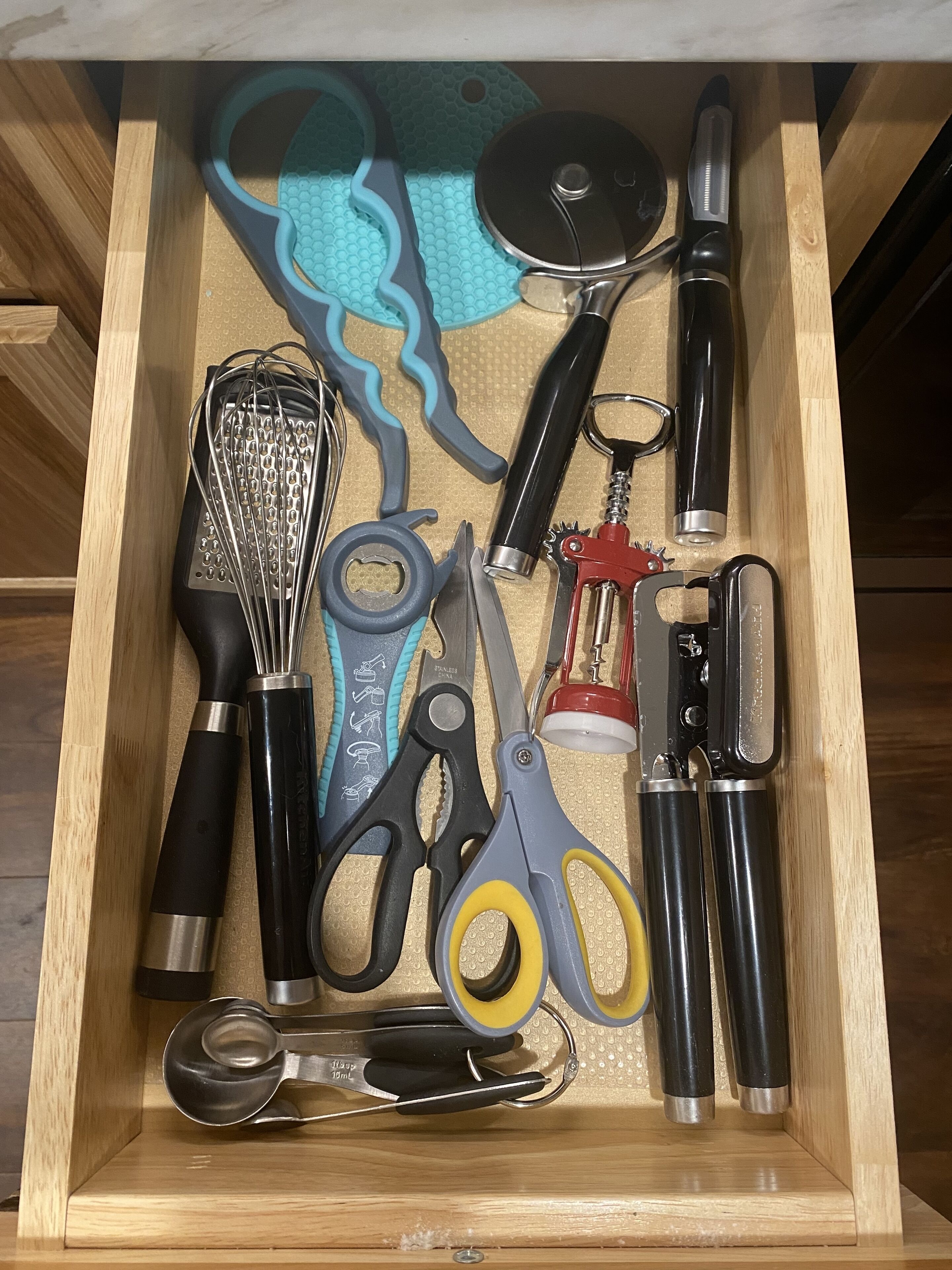 A drawer containing various kitchen utensils including a whisk, scissors, and a bottle opener.