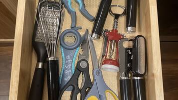 A drawer containing various kitchen utensils including a whisk, scissors, and a bottle opener.