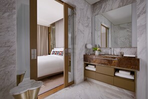 A modern hotel room with a marble floor, a large bed with a decorative pillow, a vanity with a marble countertop, and a large mirror.