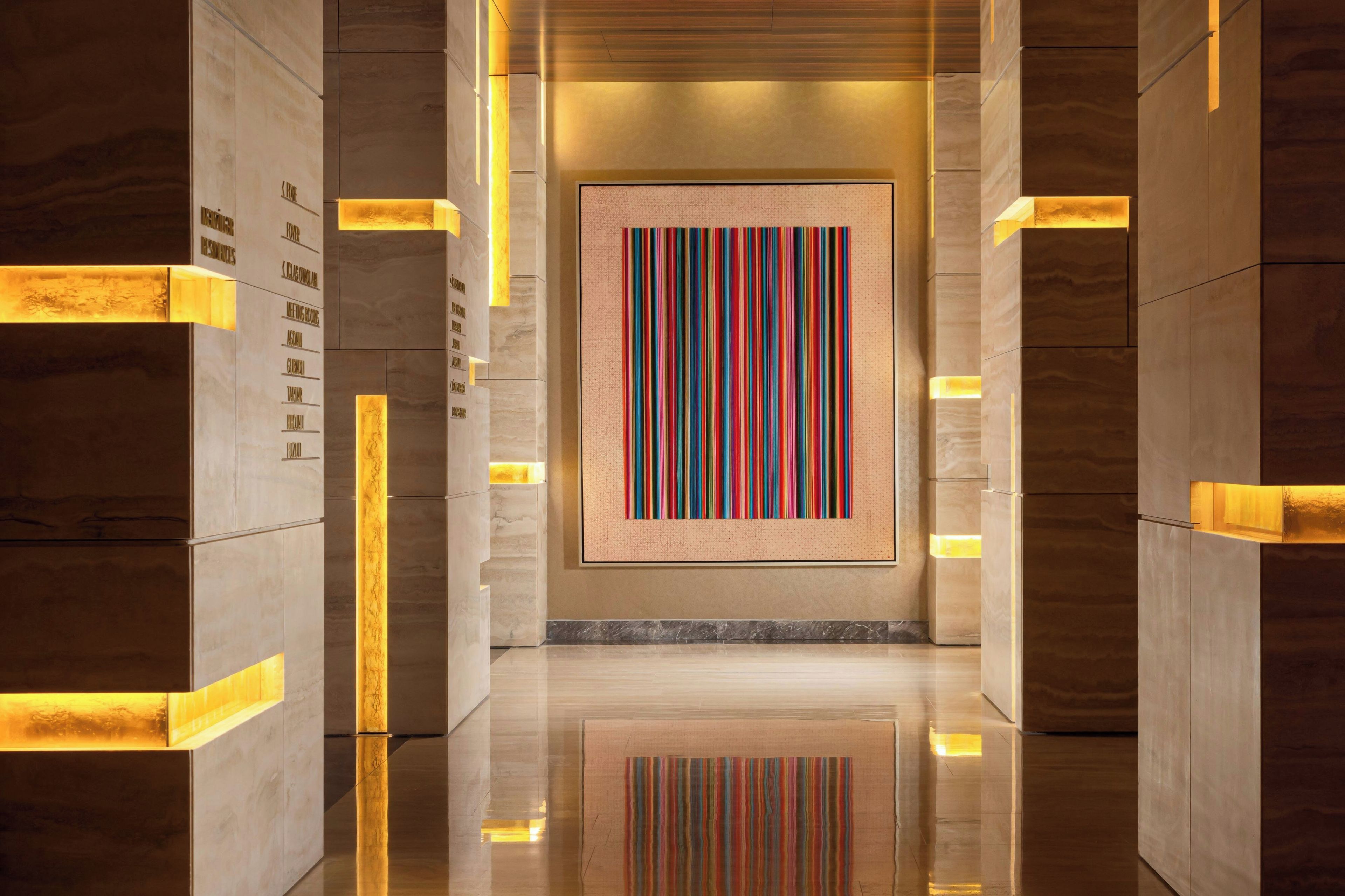 A corridor with a central artwork, marble walls, and illuminated panels.