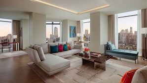 A modern living room with a sectional sofa, a coffee table, and a view of the cityscape through large windows. - The Ritz-Carlton, Baku (Baku)