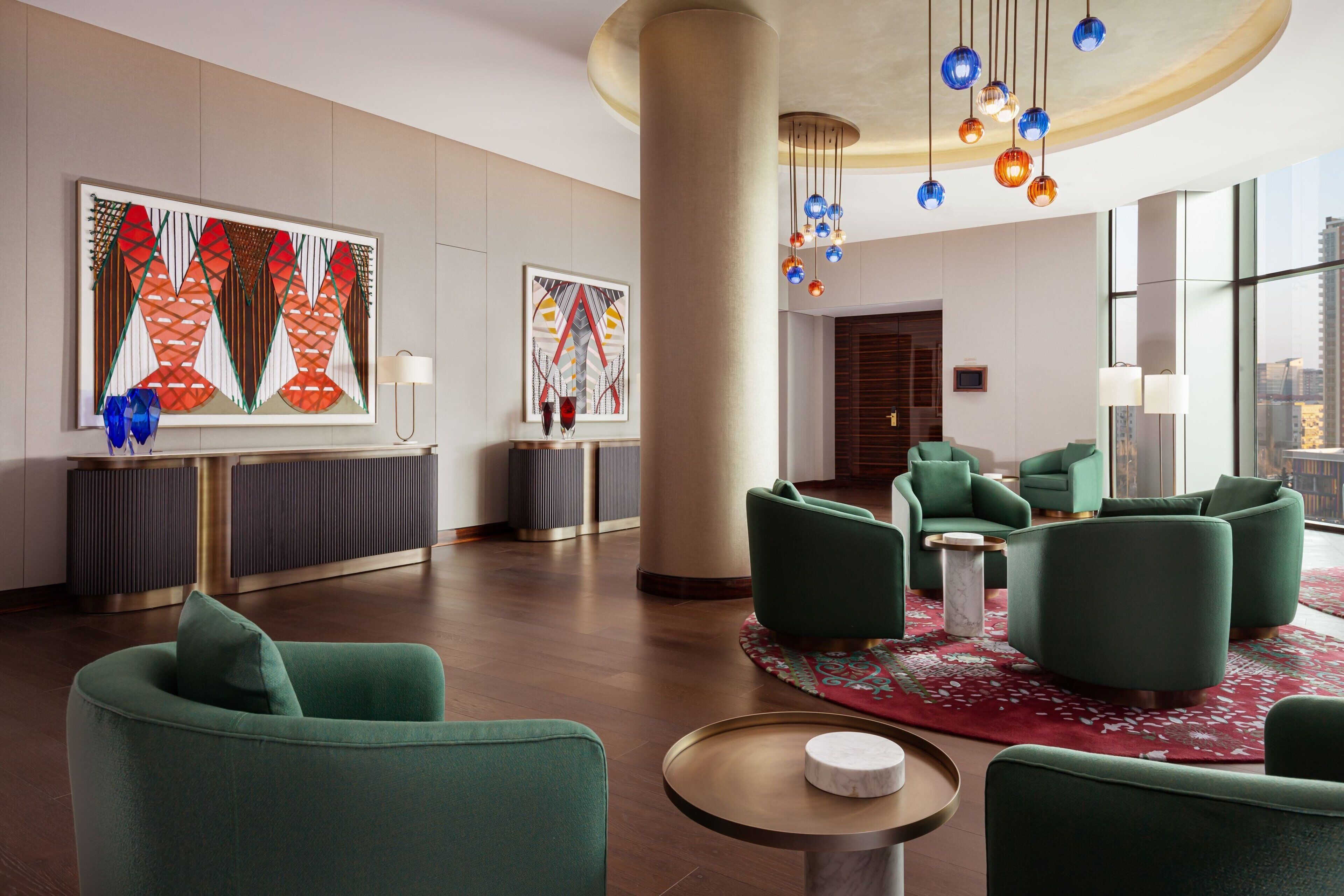 Un moderno vestíbulo de hotel con asientos tapizados en verde, grandes pinturas abstractas y una alfombra roja con estampado.