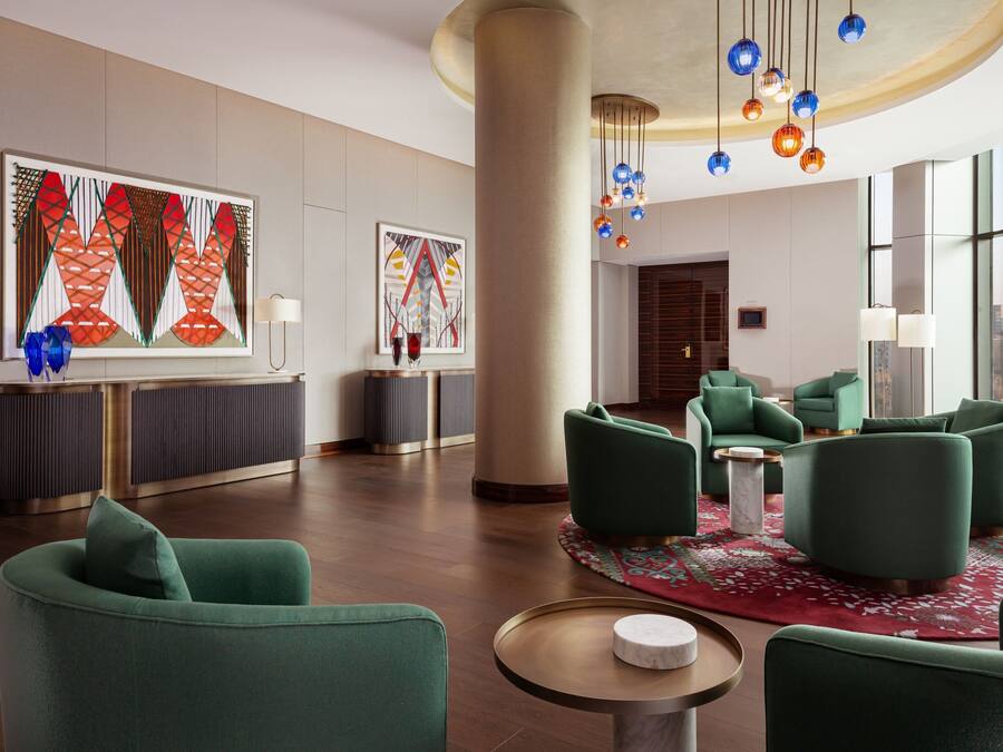 Un moderno vestíbulo de hotel con asientos tapizados en verde, grandes pinturas abstractas y una alfombra roja con estampado.