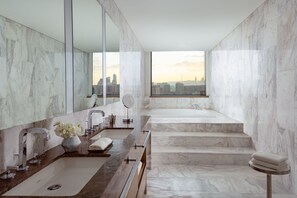 A modern bathroom with a large mirror, two sinks, a bathtub, and a view of a cityscape through a large window.