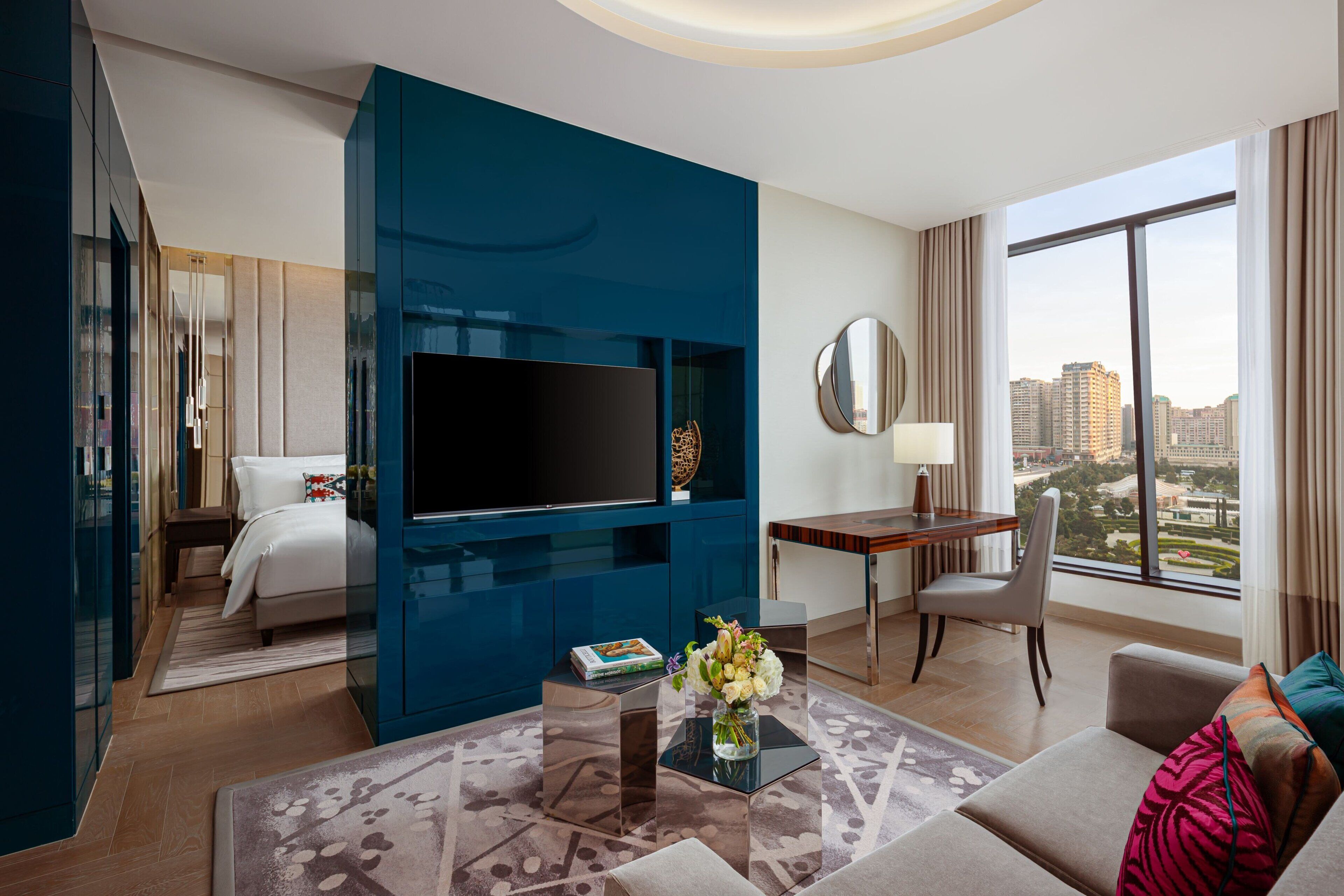 A modern hotel room with a large TV, a desk, a comfortable sofa, and a view of the city.