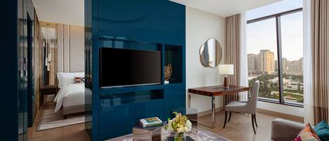 A modern hotel room with a large TV, a desk, a comfortable sofa, and a view of the city.