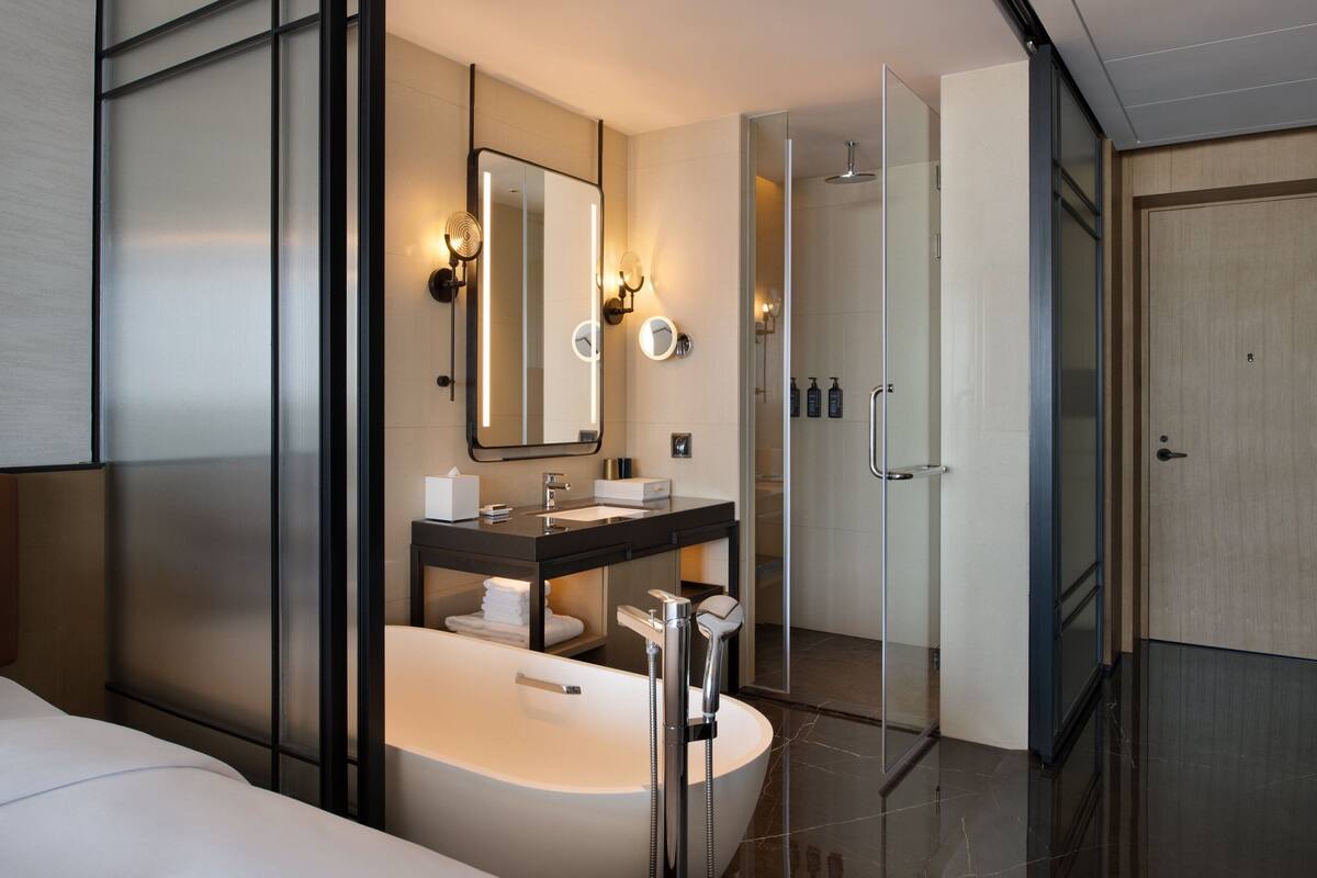 Ein modernes Badezimmer mit einer großen Badewanne, einem Waschtisch mit Spiegel und einer Duschkabine aus Glas.