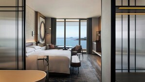Una habitación de hotel moderna con una cama grande, una zona de estar, una mesita y vistas al mar.