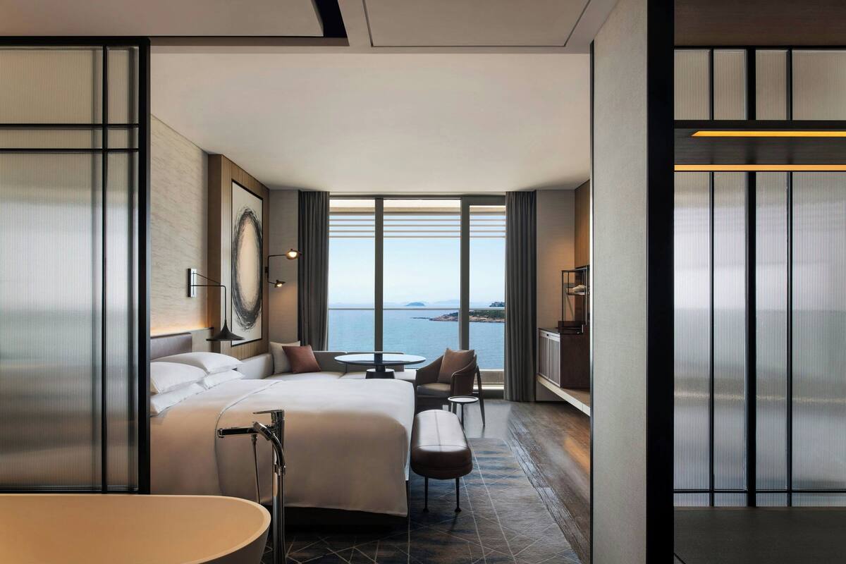 Ein modernes Hotelzimmer mit einem großen Bett, einer Sitzecke, einem kleinen Tisch und Meerblick.