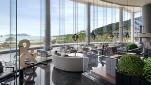 Un área de lounge moderna con una disposición curva de asientos, ventanas amplias que ofrecen vistas al paisaje y un logo 'R' destacado.