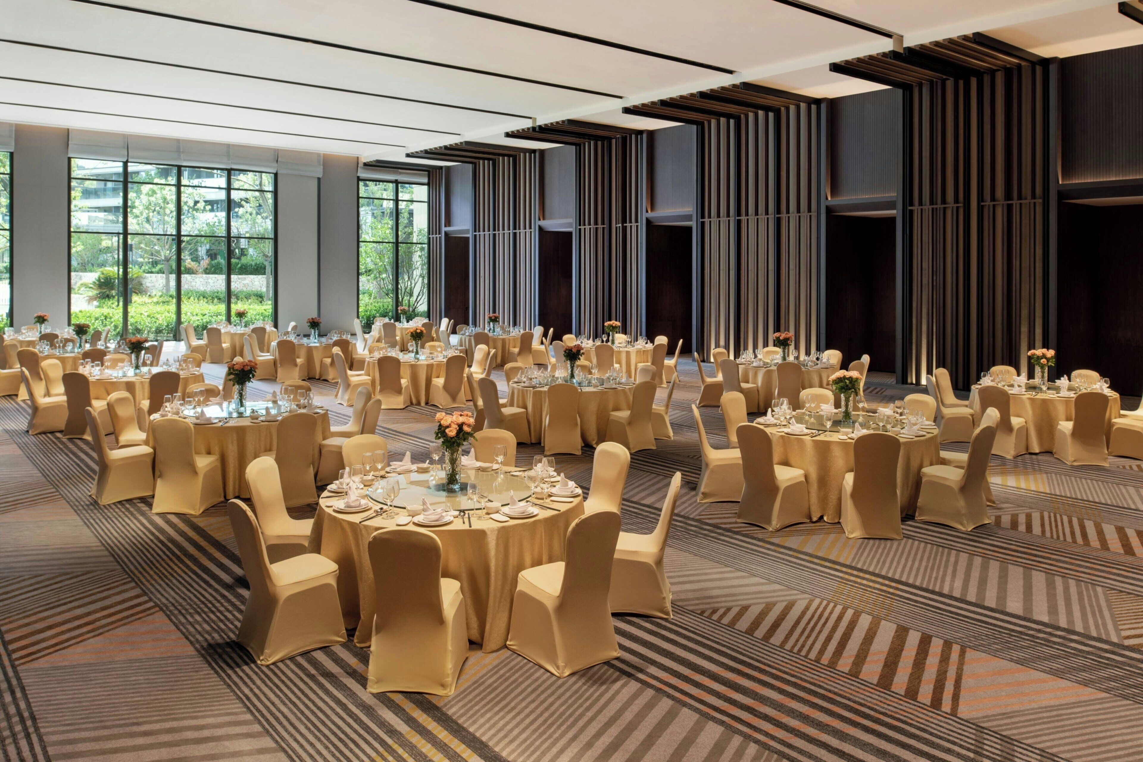 A large banquet hall with round tables, beige chairs, and a carpeted floor.