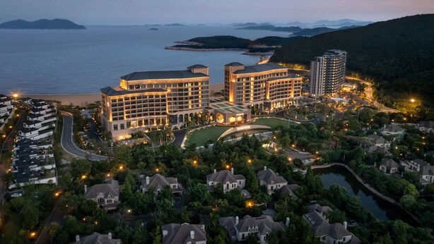Un resort con varias edificaciones, un campo de golf y una masa de agua al fondo.