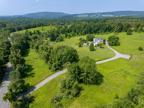 An aerial view of a rural property with a winding road, a large house, and surrounding greenery.
