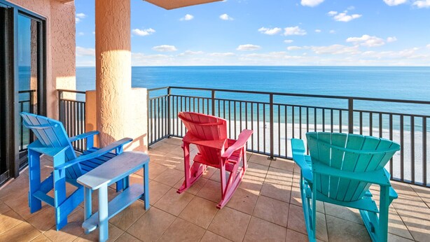 Un balcón con cuatro sillas Adirondack y una mesita, con vista a una playa y el océano.