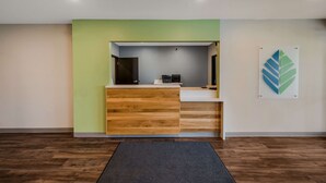 Een receptiebalie met een houten afwerking, een grijze muur achter deze balie en een groene accentmuur.
