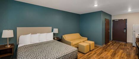 A hotel room with a large bed, a sofa, and a small table with a lamp.