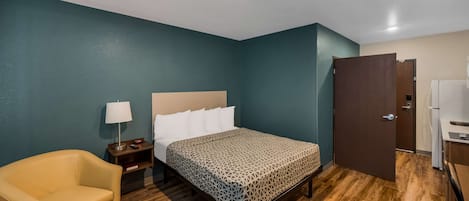 Et hotelværelse med seng, stol, natbord, lampe og garderobeskab.