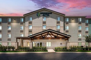 Ein Hotel mit modernem Design, das eine markante Eingangspartei mit überdachtem Gang und einem Schild mit der Aufschrift "Woodspring Suites" zeigt.