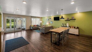 Een moderne woonkamer met een houten eettafel, banken en een aan de muur bevestigde televisie.