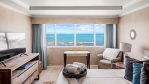 A hotel room with a large window offering a view of the ocean, a bed, a desk, a chair, and a television.