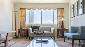 A living room with a sofa, a blue armchair, a coffee table, and a window with curtains.