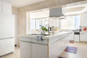 Una cocina moderna con una isla central, armarios blancos y un amplio ventanal que proporciona luz natural.