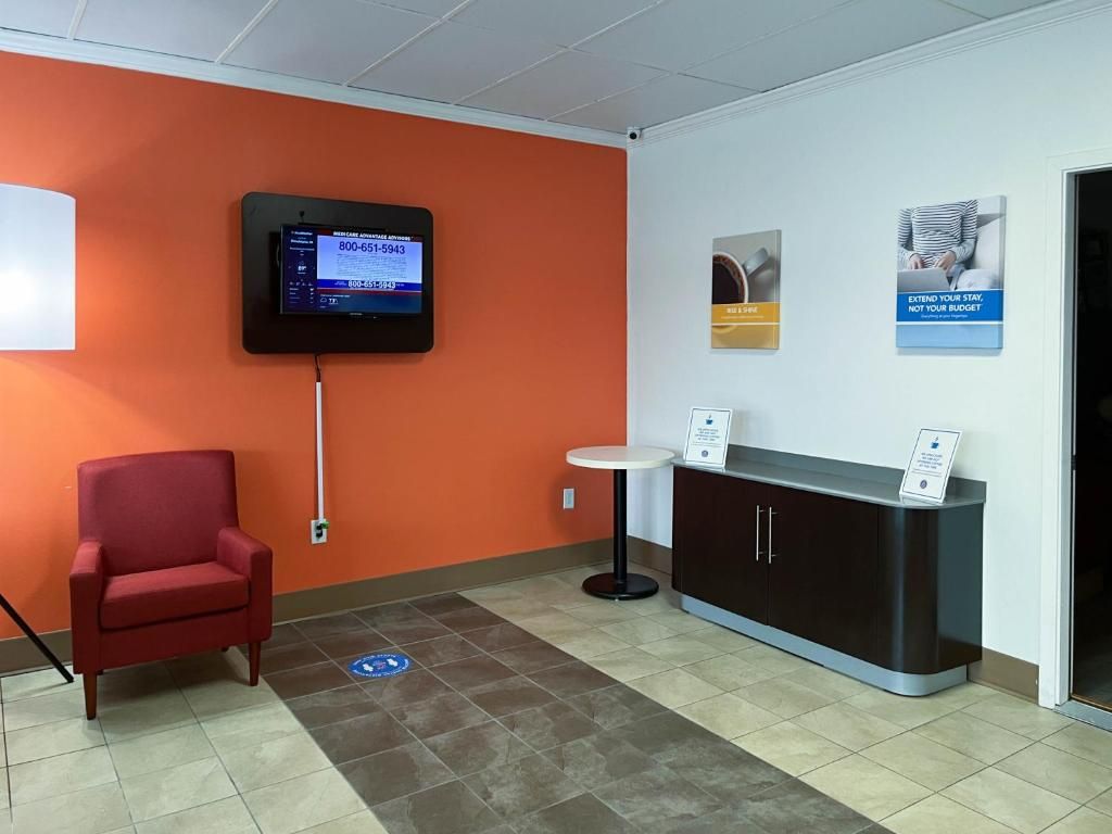 A reception area with a red chair, a black reception desk, a mounted screen, and informational posters on the wall.