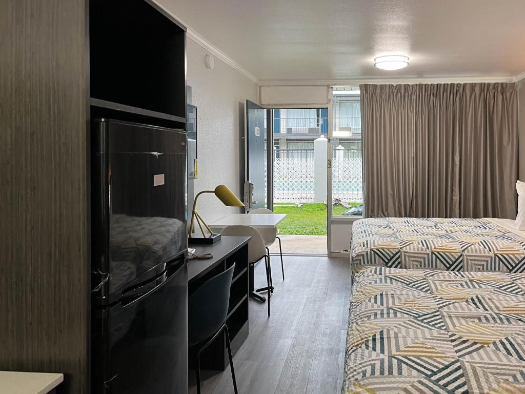 A hotel room with a bed, a desk, a chair, a television, and a sliding door leading to a balcony.