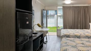 A hotel room with a bed, a desk, a chair, a television, and a sliding door leading to a balcony.