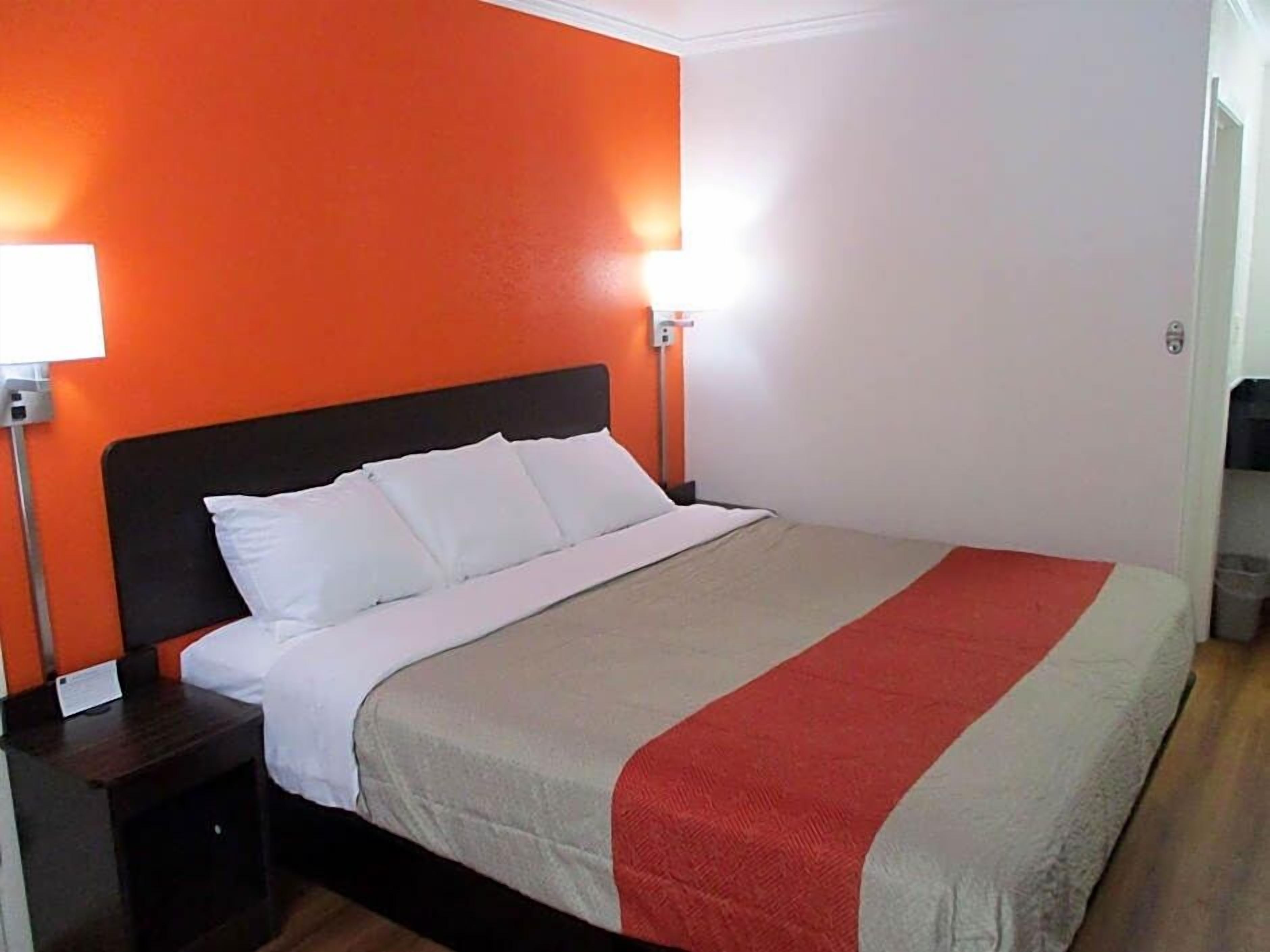 Una habitación de hotel con una cama, dos mesitas de noche y un buró.