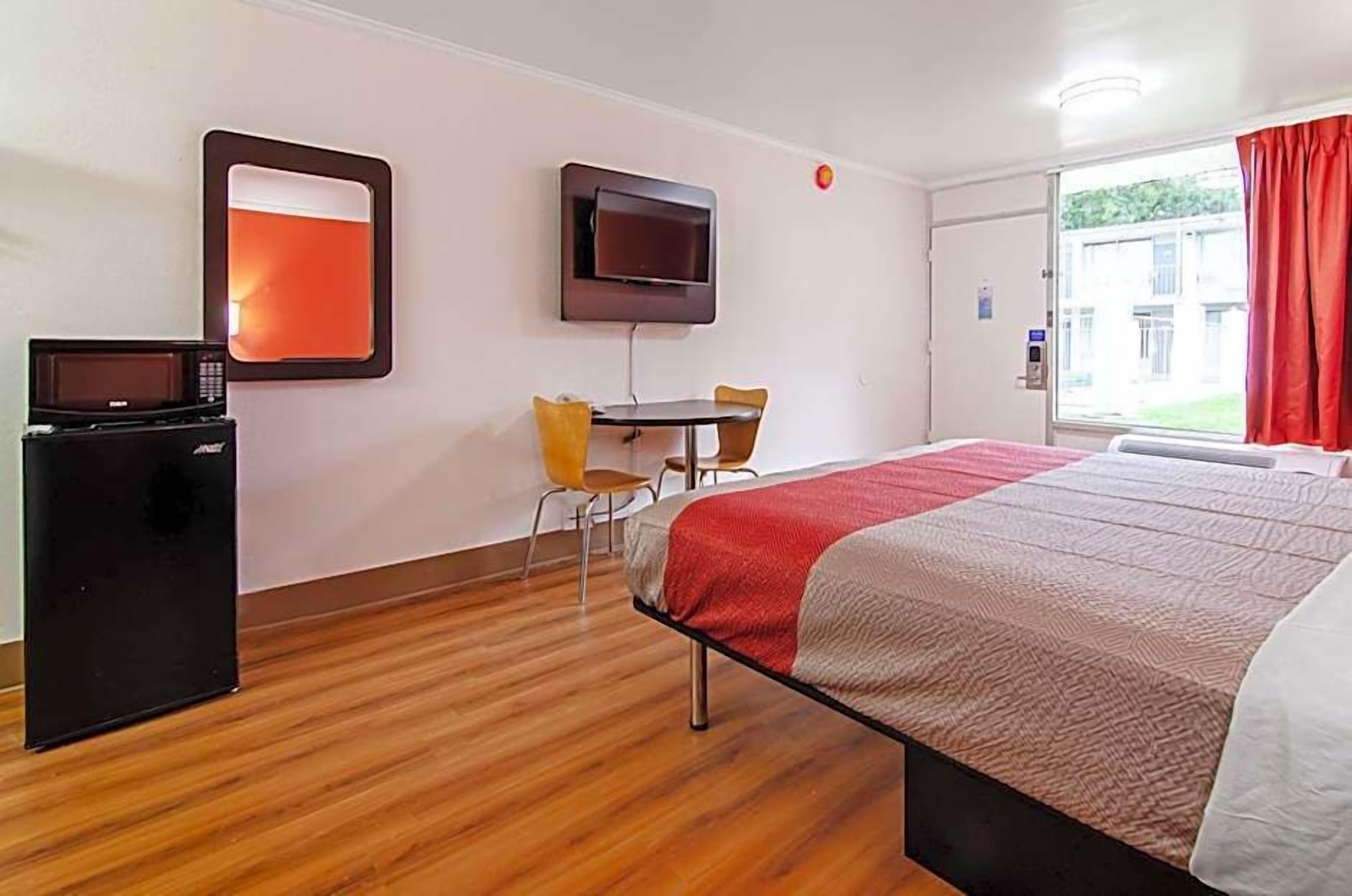A hotel room with a bed, a desk, a chair, a TV, and a microwave.