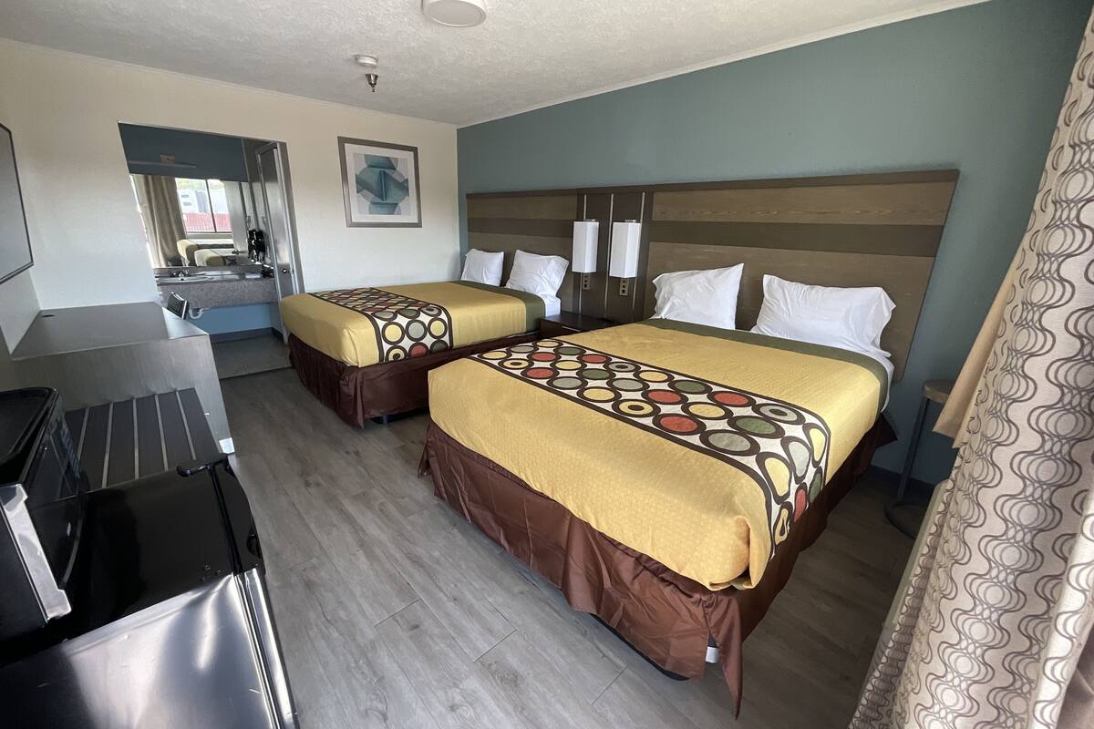 A hotel room with two beds, a kitchenette, a bathroom, and a shower area.
