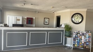 A reception area with a counter, a clock, a framed picture, a plant, and a display of magazines. - Executive Inn & Suites (Beaumont)