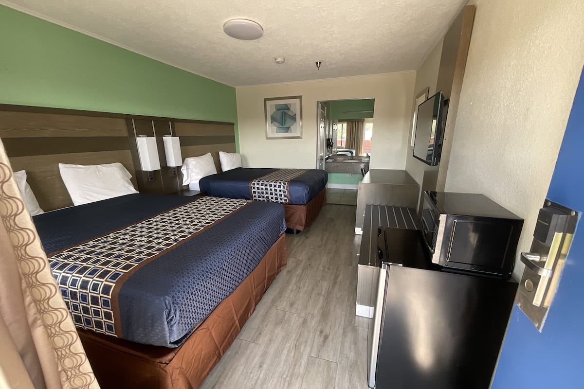 A hotel room with two beds, a kitchenette, a bathroom, and a TV.