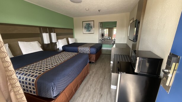 A hotel room with two beds, a kitchenette, and a bathroom visible in the background. - Executive Inn & Suites (Beaumont)