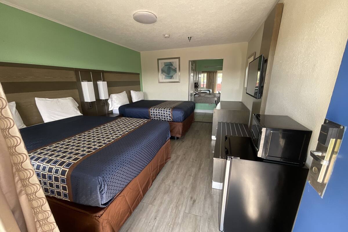 A hotel room with two beds, a kitchenette, and a bathroom visible in the background.