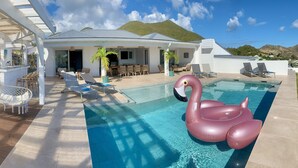 Un área de piscina con un flotador con forma de cisne, mobiliario exterior y un porche cubierto.