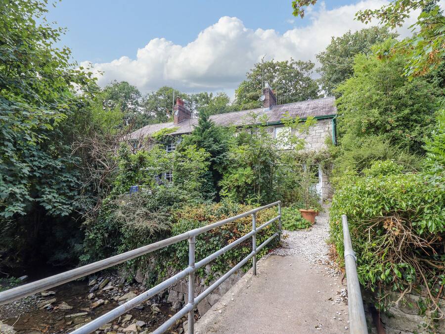 A stone building with a green roof, surrounded by dense foliage and a gravel path leading to it.